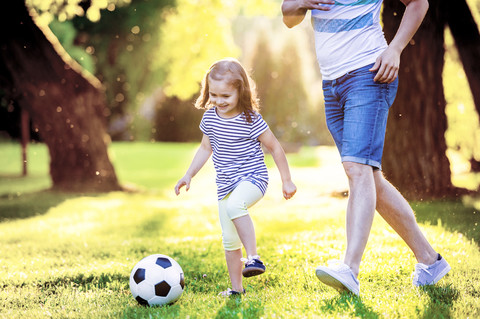 Glückliches kleines Mädchen, das mit seinem Vater in einem Park Fußball spielt, lizenzfreies Stockfoto