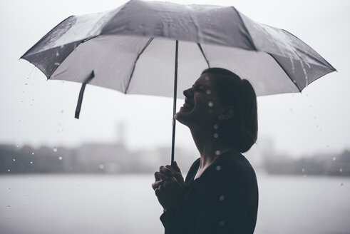 Lachende Frau mit Regenschirm an einem regnerischen Tag - DASF000050