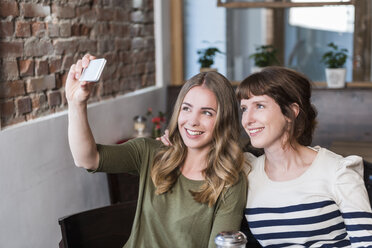 Two best friends sitting in a coffee shop taking selfie with smartphone - KAF000171