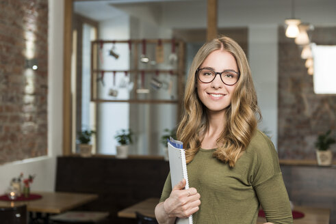 Porträt einer lächelnden blonden Frau mit Notizbuch in einem Café - KAF000172