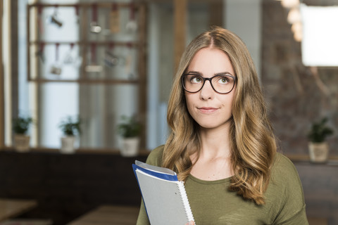 Porträt einer skeptischen blonden Frau mit Notizbuch in einem Café, lizenzfreies Stockfoto