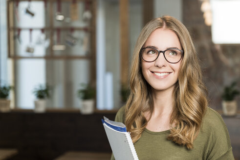 Porträt einer lächelnden blonden Frau mit Notizbuch in einem Café - KAF000174