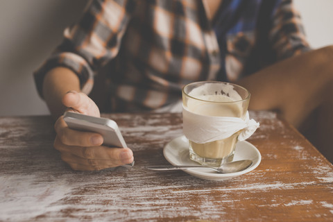 Frau überprüft Mobiltelefon in einem Café, lizenzfreies Stockfoto