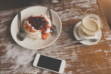 Pavlova dessert, cell phone and coffee on table - KNTF000407