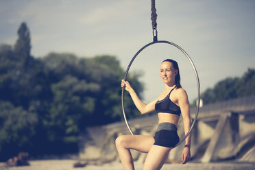 Sportive young woman sitting in hoop swing - YNF000009