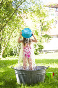 Kleines Mädchen, das in einer Wanne auf einer Wiese steht und sich mit Wasser übergießt - LVF005052