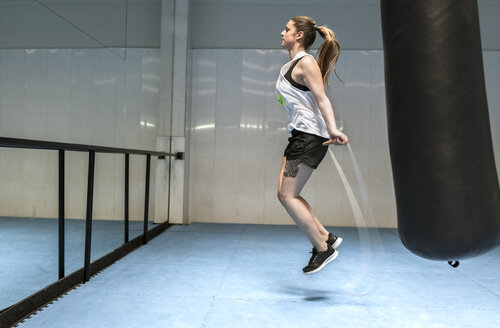 Junge Frau im Fitnessstudio, die Seil springt - MGOF002028