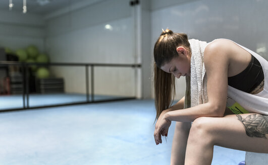 Junge Frau sitzt im Fitnessstudio nach dem Training - MGOF002033
