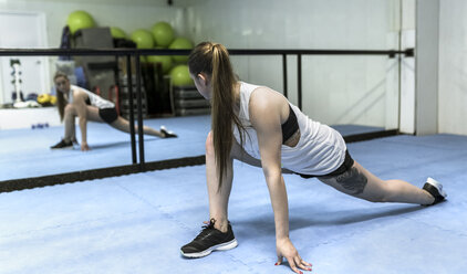 Junge Frau macht Dehnungsübungen im Fitnessstudio - MGOF002035