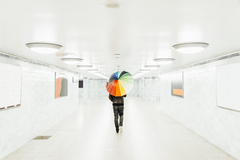 Mann mit buntem Regenschirm geht durch einen leeren U-Bahn-Tunnel in Berlin - MMF001285
