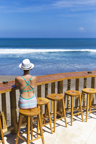 Indonesien, Bali, Junge Frau sitzt auf Barhocker am Strand, lizenzfreies Stockfoto