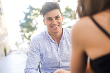 Porträt eines lächelnden jungen Mannes, der mit seiner Freundin in einem Straßencafé sitzt - SIPF000581