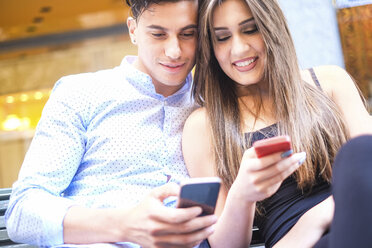 Porträt eines jungen Paares, das auf einer Bank sitzt und auf seine Smartphones schaut - SIPF000582