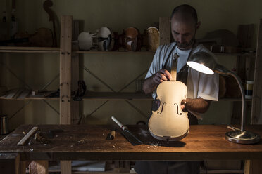 Geigenbauer bei der Prüfung einer Geige in seiner Werkstatt - ABZF000771