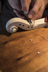 Luthier using a chisel on a violin scroll during the manufacture of a violin in his workshop - ABZF000774