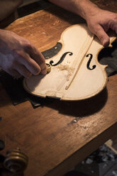 Luthier using a mini hand plane on the top plate of a violin in his workshop - ABZF000776