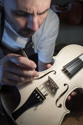 Geigenbauer bei der Untersuchung des Stimmstocks einer unlackierten Geige in seiner Werkstatt - ABZF000781