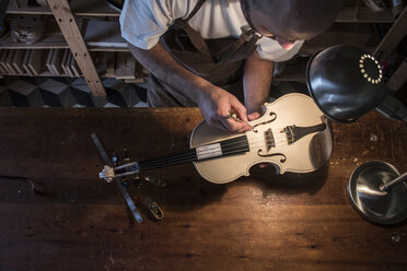 Luthier adjusting the sound post of an unvarnished violin in his workshop - ABZF000785