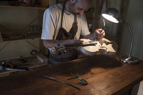 Geigenbauer beim Einstellen des Stimmstocks einer Geige in seiner Werkstatt, lizenzfreies Stockfoto