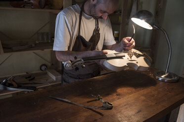 Luthier adjusting the sound post of a violin in his workshop - ABZF000786