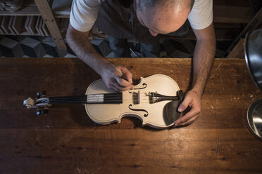 Luthier adjusting the sound post of an unvarnished violin in his workshop - ABZF000790