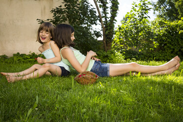 Two laughing sisters sitting back to back on a meadow - LVF005083