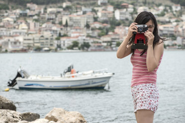 Greece, Amfilochia, woman taking picture at the sea with vintage camera - DEGF000877