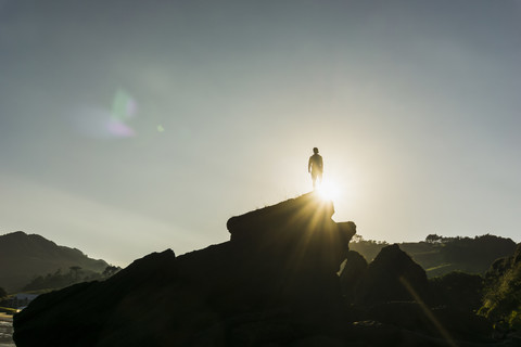 Silhouette eines auf einem Felsen stehenden Mannes bei Gegenlicht, lizenzfreies Stockfoto