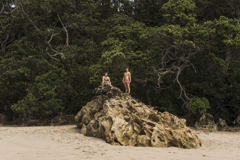 Neuseeland, zwei Freunde auf einem großen Felsen am Strand, lizenzfreies Stockfoto