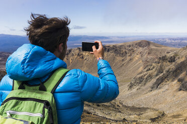 New Zealand, Tongariro National Park, back view of hiker taking a photo with smartphone - UUF007948