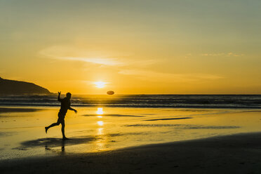 Silhouette of man on the beach playing with frisbee at twilight - UUF007962