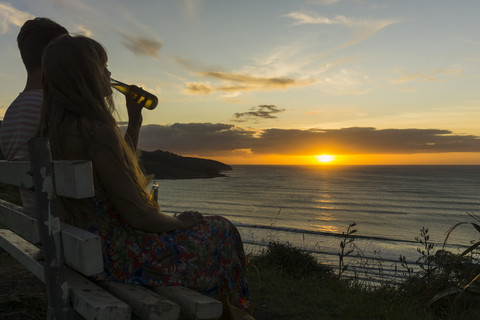 Paar sitzt bei Sonnenuntergang auf einer Bank und trinkt Getränke in Glasflaschen, lizenzfreies Stockfoto