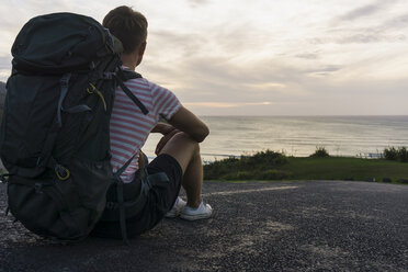 Back view of sitting hiker with backpack looking to the sea - UUF007968