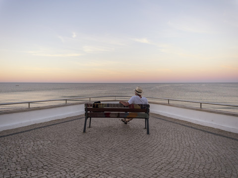 Portugal, Senior man siting on bench watching sunrise stock photo