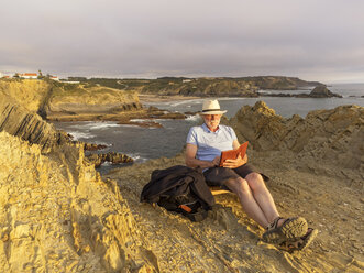 Portugal, älterer Mann sitzt am Strand und liest ein Buch - LAF001666