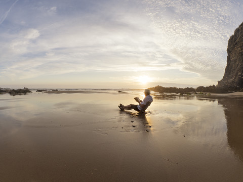 Portugal, älterer Mann sitzt am Strand und liest ein Buch, lizenzfreies Stockfoto