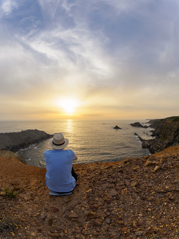 Portugal, älterer Mann sitzt in der Bucht und beobachtet den Sonnenuntergang, lizenzfreies Stockfoto