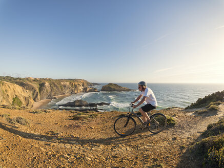 Portugal, Senior man mountain biking at the sea - LAF001680
