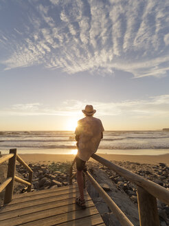 Portugal, Senior man sitting on railing at the beach - LAF001686