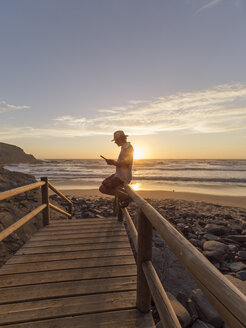 Portugal, älterer Mann sitzt auf dem Geländer am Strand und liest - LAF001687