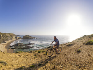 Portugal, Senior man mountain biking at the sea - LAF001693