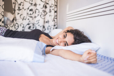 Portrait of smiling teenage girl lying on bed stretching her arm - SIPF000597