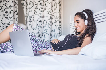 Teenager-Mädchen mit Kopfhörern auf dem Bett liegend mit Laptop - SIPF000598