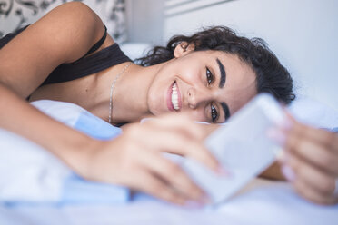 Teenage girl lying on bed looking at her smartphone - SIPF000600