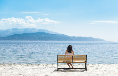 Greece, Sergoulas, woman sitting on bench at the coast - DEGF000899