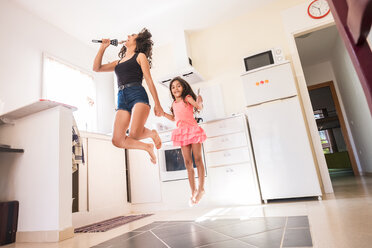 Verspieltes Mädchen im Teenageralter mit ihrer kleinen Schwester in der Küche, die so tut, als würde sie ins Mikrofon singen - SIPF000632