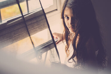 Porträt eines kleinen Mädchens mit langen Haaren, das am Fenster steht - SIPF000637