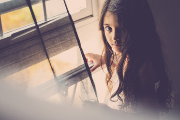 Portrait of little girl with long hair standing near window - SIPF000637