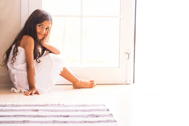 Porträt eines lächelnden kleinen Mädchens, das auf dem Boden vor einer Balkontür sitzt - SIPF000639