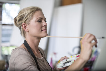 Frau in ihrem Heimatelier, die malt und eine Palette in der Hand hält - ZEF008878